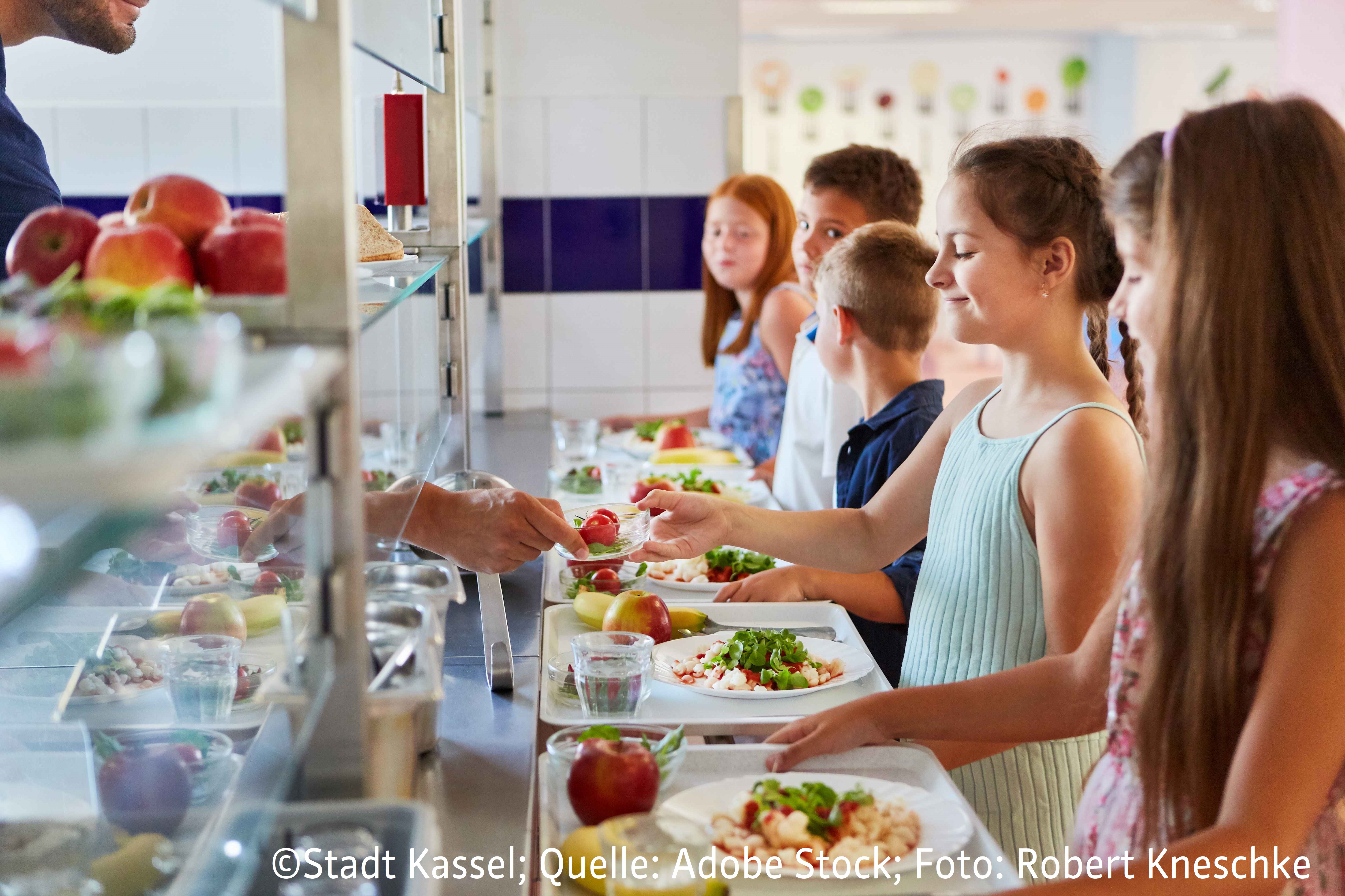 Mehrere Grundschüler, die in einer Mensa für ihr Mittagessen anstehen.