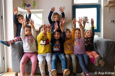 Eine Kindergruppe steht auf einem Sofa und streckt jubelnd die Hände in die Höhe